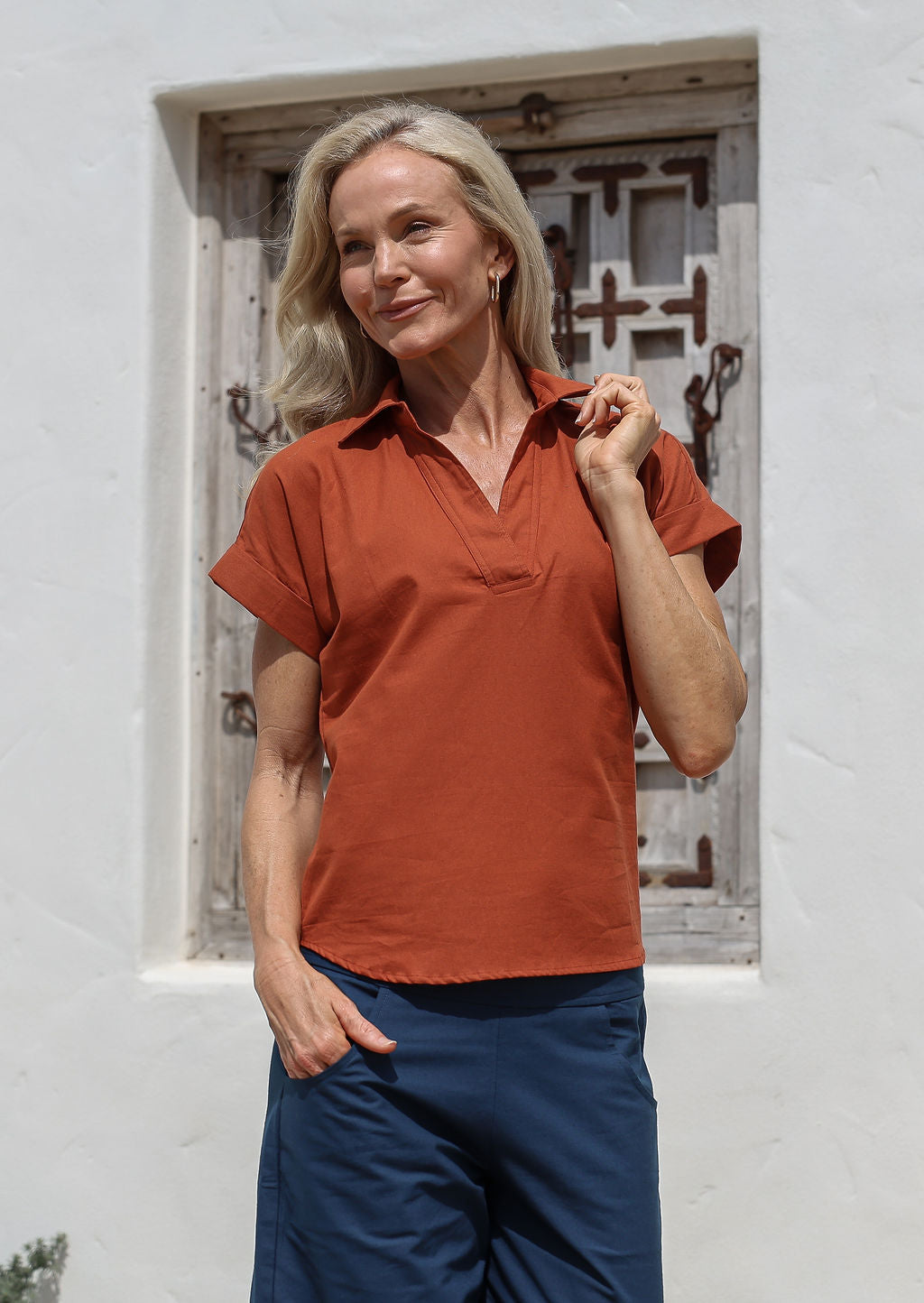 Woman wearing a rust-colored shirt style cotton top with V-neckline and short folded cuff sleevesa