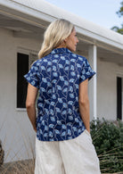 Woman standing backwards wearing a floral cotton top with short folded cuff sleeves, collar and V neckline