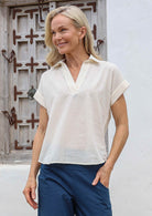 Woman wearing a natural white cotton top with structured collar, relaxed fit and short folded cuff sleeves.