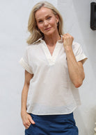 Woman wearing loose cut 100% cotton shirt style top with collar, V-neckline and folded cuff sleeves 