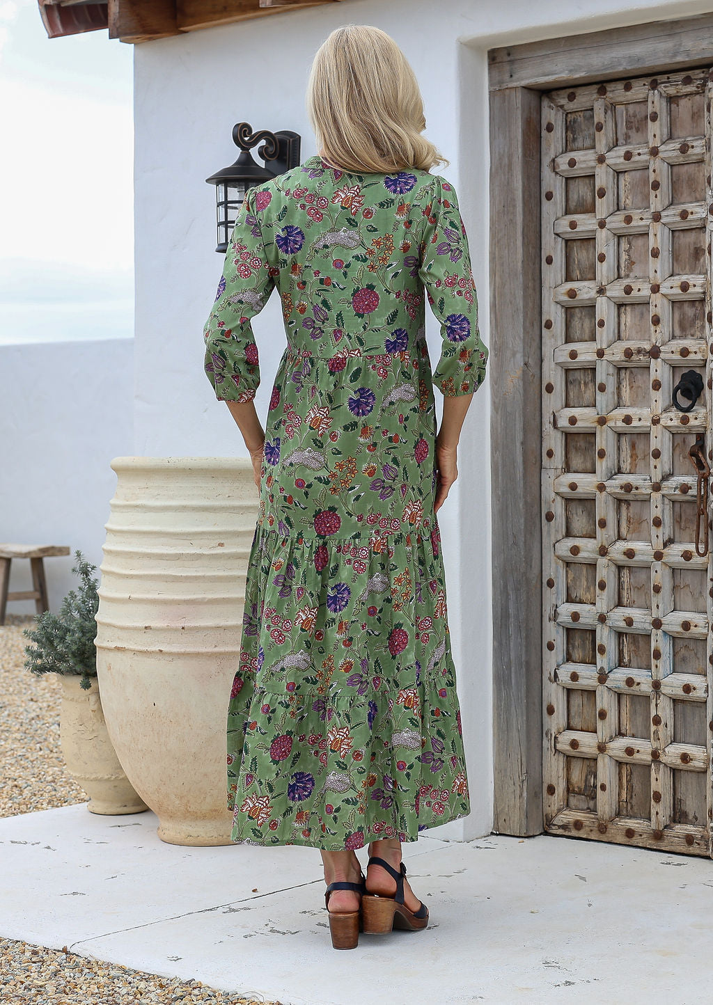 Woman standing in a moss green based floral cotton maxi dress with a three-tiered design, pockets, and 3/4 sleeves.