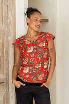 Model posing in a red based floral print tailored cotton top with cap sleeves, round neckline and length sitting at the hip 