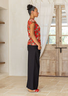 A woman stands sideways wears a 100% cotton tailored top with short cap sleeves and a round neckline with a keyhole cutout, paired with black cotton pants