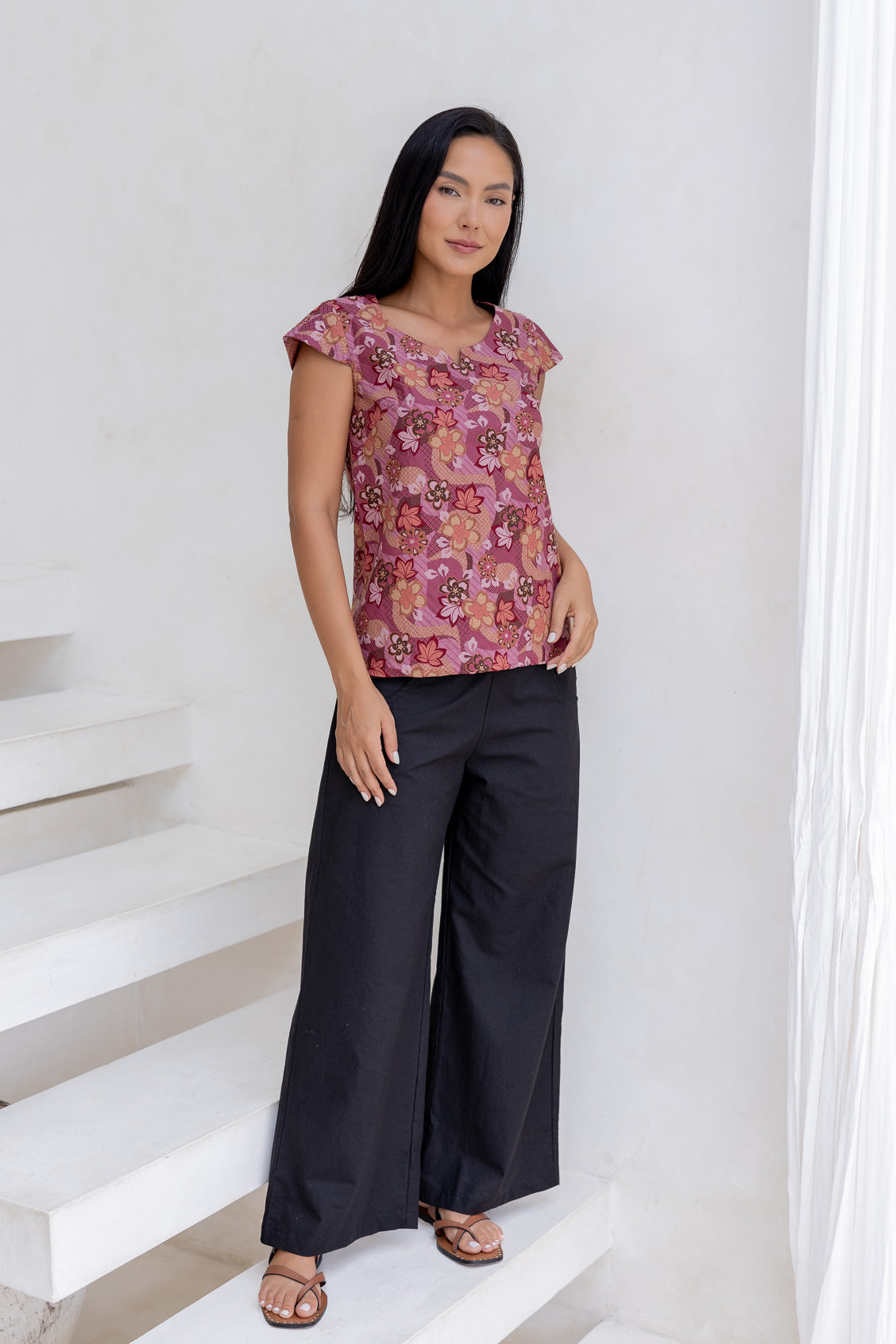 Woman standing in a 100 percent cotton floral print top with cap sleeves, round neckline and keyhole cutout.