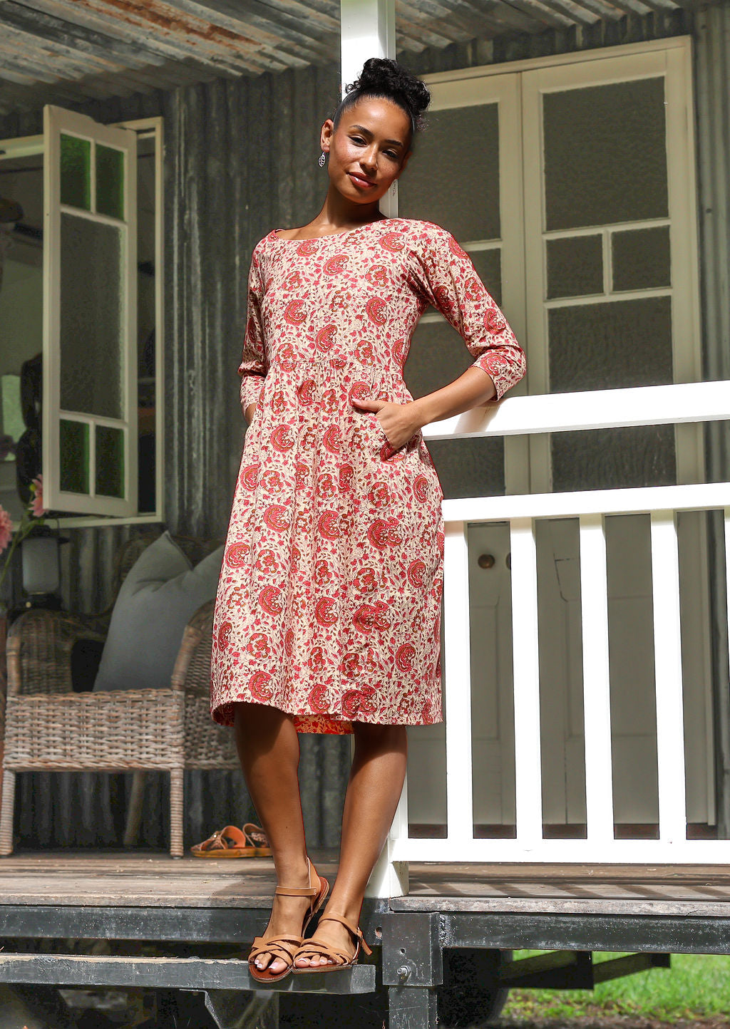 Woman in cream based floral print, knee length sundress with sleeves,  with hand in pocket