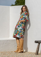 Woman standing sideways wearing a knee length sundress with colourful floral print