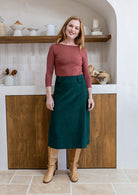 Woman in a terracotta top and green cotton corduroy A-line midi length skirt with belt loops
