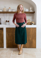 Woman in a green cotton corduroy A-line midi length skirt with belt loops 