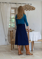 Woman stands backwards wearing a cotton corduroy skirt in navy blue with belt loops and a side zip.