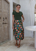 Woman wearing a knee length, box pleated cotton skirt with button front, belt loops and pockets.