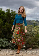 Woman in a cotton velvet floral skirt and blue top standing outdoors with trees. 