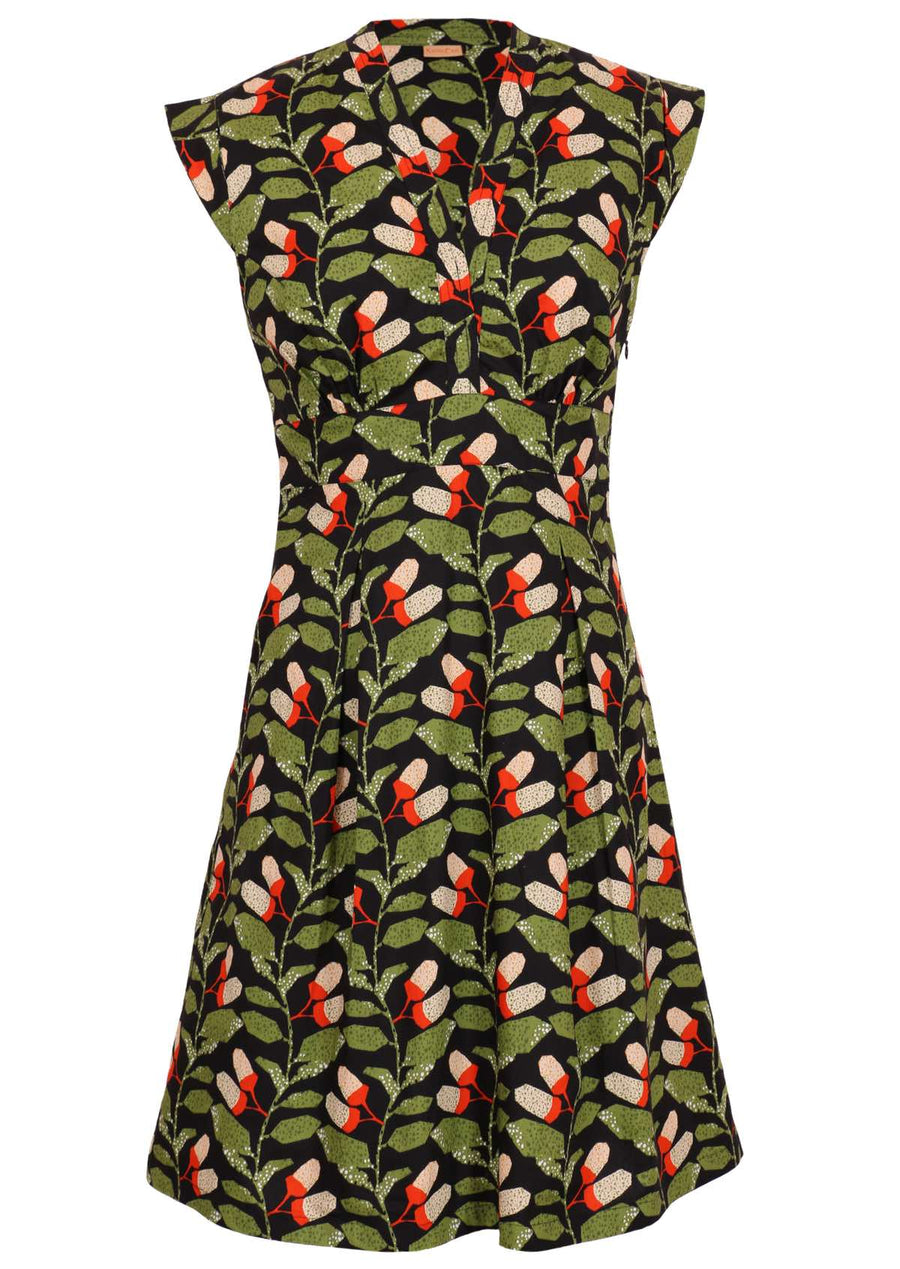 Model wears Billie Dress Oak green, orange- white speckled botanical print on black base cotton V-neck cap sleeves box pleats at waist form A-line skirt side zip knee length 