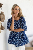 Woman standing wearing a 100% cotton top in navy based floral print paired with white plain pants