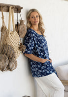 Woman standing wearing a 100% cotton top in navy based floral print with short sleeves and front pockets 