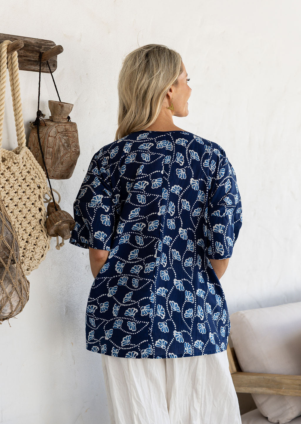 Woman standing backwards wears a navy based floral print 100% cotton relaxed fit top with short sleeves and front pockets