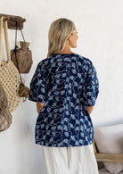 Woman standing backwards wears a navy based floral print 100% cotton relaxed fit top with short sleeves and front pockets