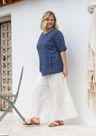 Woman stands sideways wears a navy and white striped 100% cotton relaxed fit top with an asymmetrical hem line and front pockets. 
