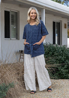 Woman wears a navy and white striped 100% cotton relaxed fit top with an asymmetrical hem line and front pockets paired with white pants