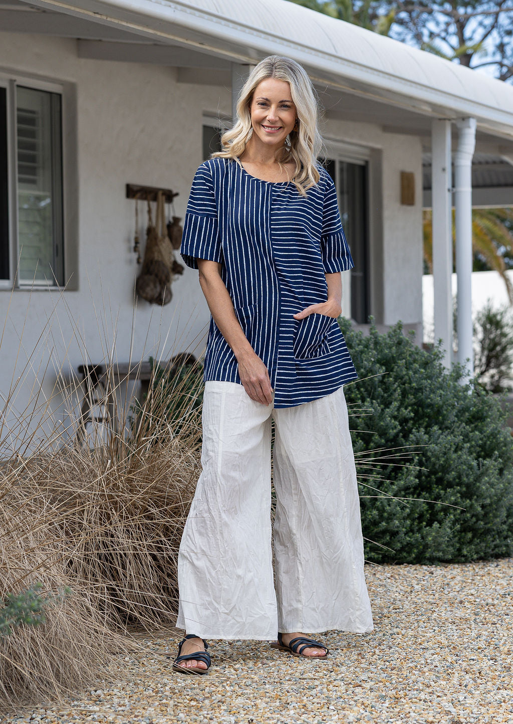 Woman standing wearing a 100% cotton top in navy and white striped with short sleeves and front pockets 
