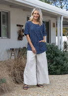Woman standing wearing a 100% cotton top in navy and white striped with short sleeves and front pockets 