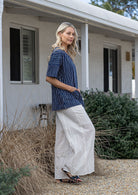 Woman standing sideways wearing a 100% cotton top in navy and white striped with both hand in pockets paired with white plain pants