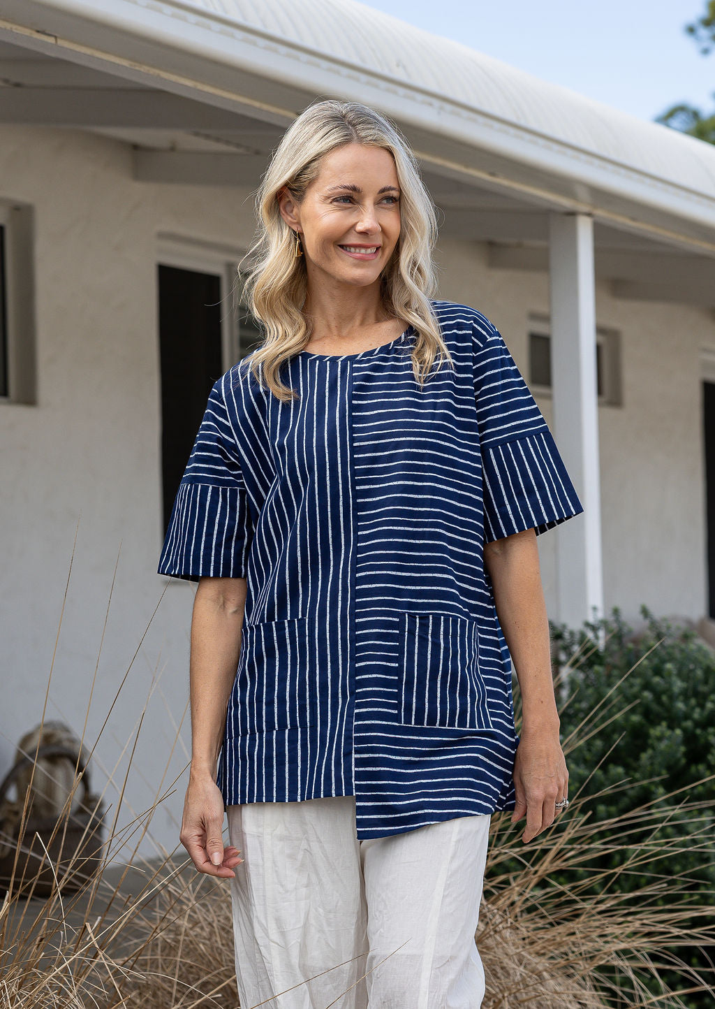 Woman wears a navy and white striped 100% cotton relaxed fit top with an asymmetrical hem line.