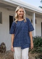 Woman wears a navy and white striped 100% cotton relaxed fit top with an asymmetrical hem line.