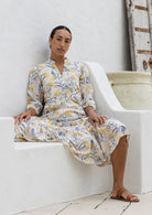 Woman in a floral dress sitting on a white bathtub in a minimalistic setting.