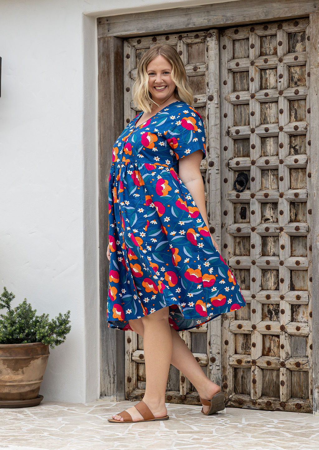 Woman standing sideways wearing a 100% cotton dress in royal blue based floral print