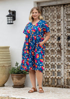 Woman in a cotton royal blue based floral button through dress with short sleeves, V-neckline and one hand in pocket