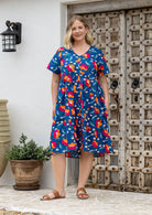 Woman wearing a royal blue based cotton floral button through dress with both hand in pockets, short sleeves and a V-neckline
