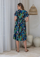 Woman in a navy based cotton floral dress standing in a room showing the back of the dress cinched with shoestring ties