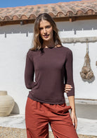 Woman wearing a brown rayon jersey top with 3/4 sleeves and a boat-neckline, paired with rust pants