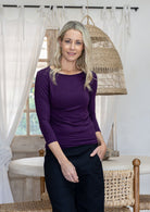 Woman wearing a rayon boat neck purple 3/4 sleeve top paired with plain black pants