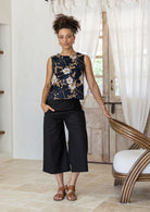Woman poses in sleeveless, relaxed fit boxy top with high round neckline, and side bust darts in floral print on a black base.
