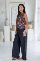 Model stands slightly sideways wearing a sleeveless floral cotton boxy top paired with black cotton pants.