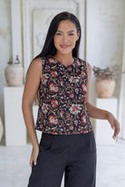 Model poses in sleeveless cotton top in black based floral print with high round neckline and side bust darts.