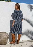 Model standing backwards wearing a relaxed fit cotton dress sitting just below the knee length in navy blue based floral print.