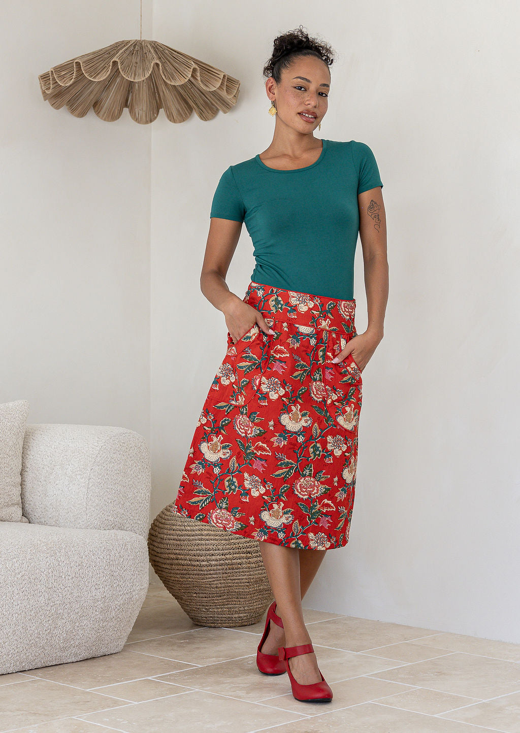 Woman posing in red based floral print cotton skirt with side zipper and piped detailing at the waistband and pockets 