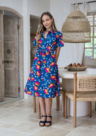 Woman wearing 100 percent cotton button through shirt dress with collar and short sleeves, in a royal blue based floral print.