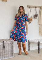 A woman wearing a short-sleeve midi dress with florals on a royal blue background