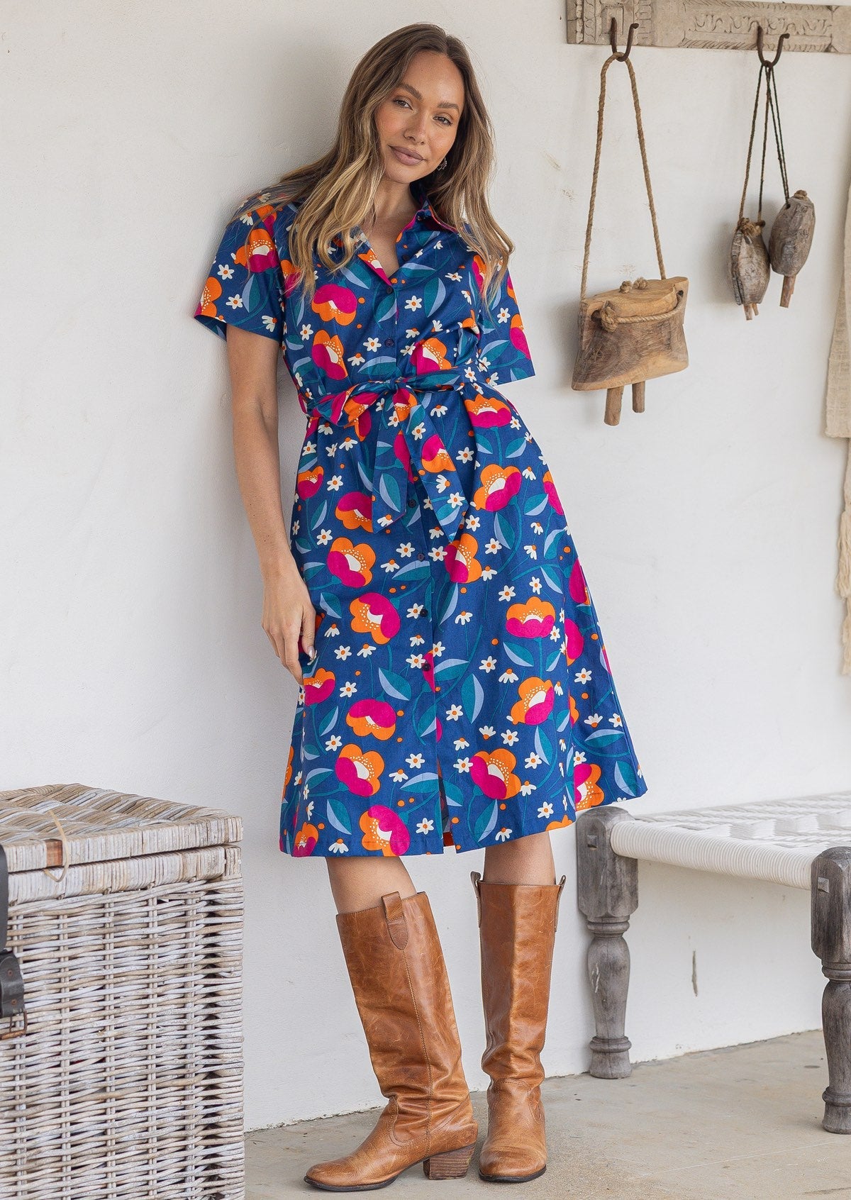 Model poses wearing a shirt style button through cotton dress with collar and a removable waist tie.