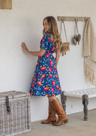 Model stands sideways wears 1950s inspired, button through shirt style dress with collar, short sleeves, waist tie and pockets.
