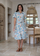 Woman wearing 100 percent cotton button through shirt dress with collar and short sleeves, in a white based floral print.