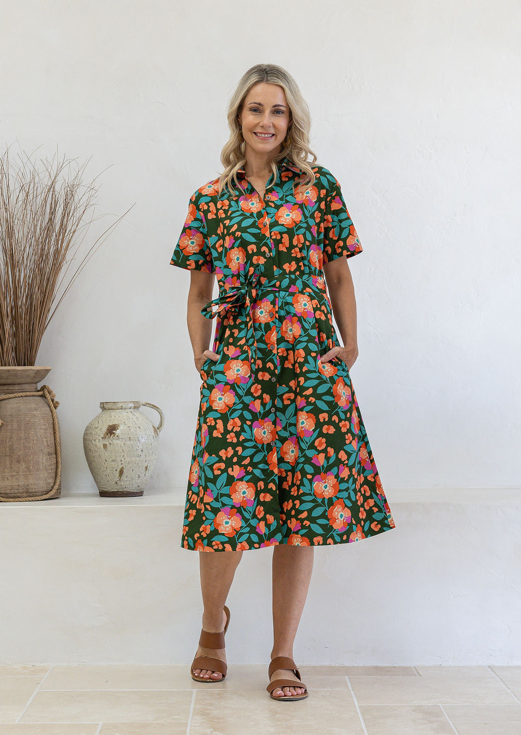Model poses wearing a shirt style button through cotton dress with collar and a removable waist tie.