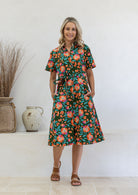 Model poses wearing a shirt style button through cotton dress with collar and a removable waist tie.