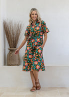 Woman standing in printed shirt dress with detachable fabric belt, short sleeves and pockets.