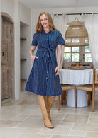 Woman wearing 100 percent cotton button through shirt dress with collar and short sleeves, in a navy based white striped print. 