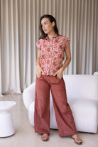 Woman wearing a 100% cotton gentle cream based floral top standing in a minimalistic room.