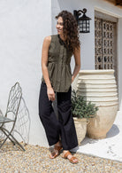 Woman wearing an olive green sleeveless cotton top and black wide-leg pants standing against a white wall.